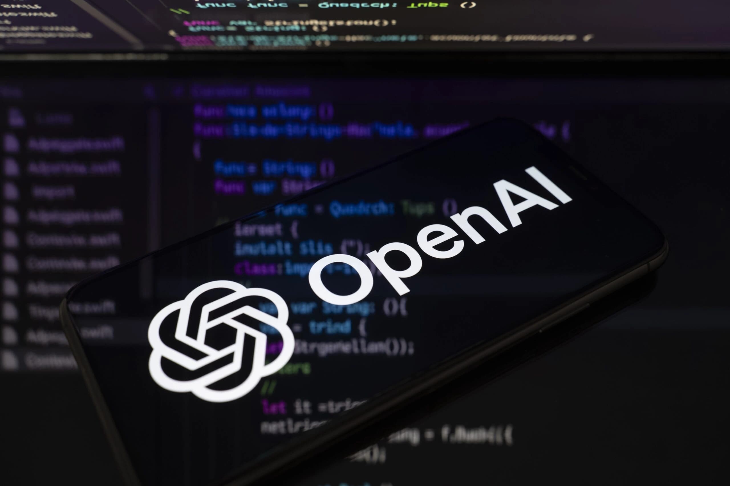 Logotipo da OpenAI em uma tela de celular sobre fundo refletivo com linhas de código projetadas